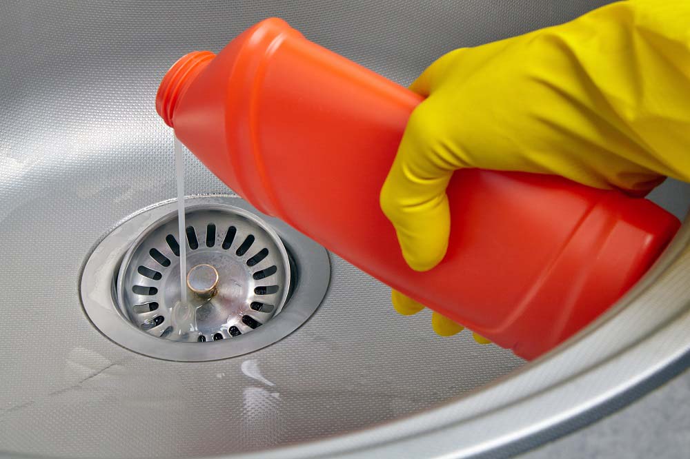 man using chemical drain cleaner to clean sink drain